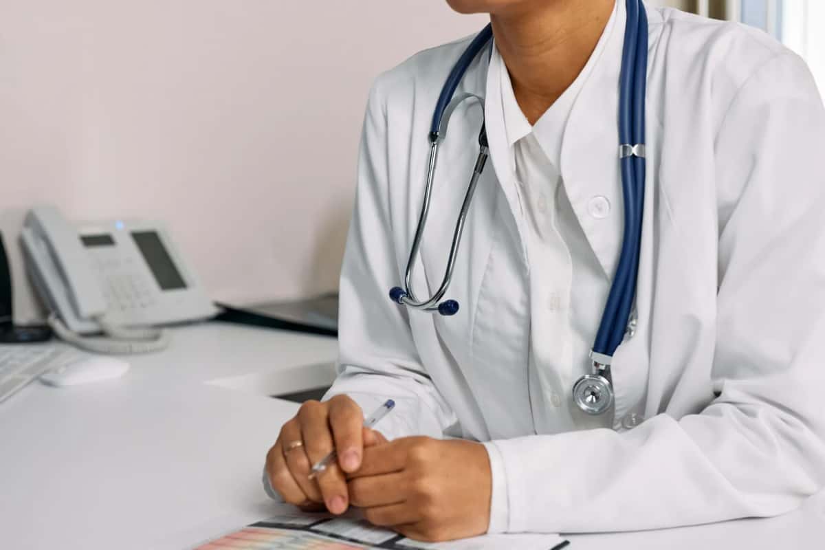Médecin en blouse blanche assis à son bureau de consultation, stéthoscope autour du cou