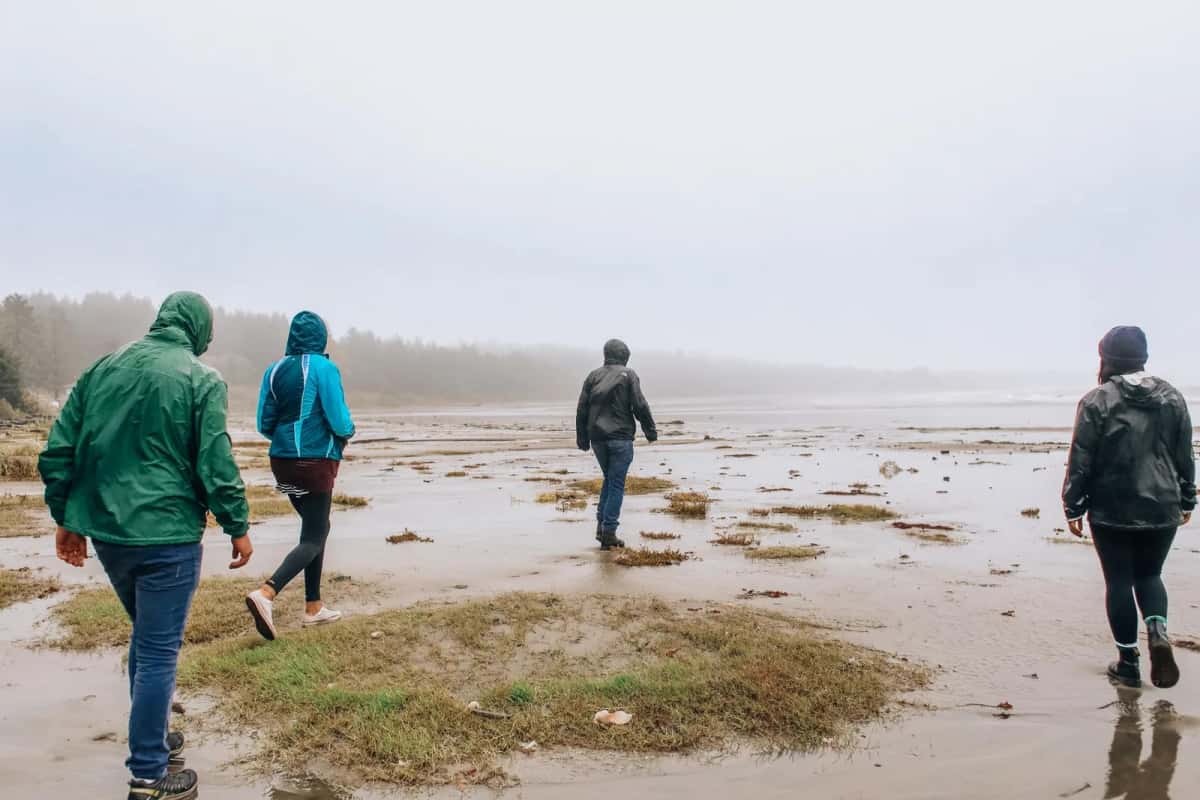 Randonneurs en imperméables marchant sur une plage sous la pluie et la brume
