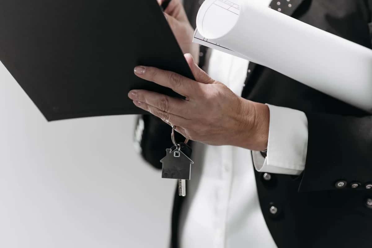Mains tenant un porte-clés en forme de maison, un porte-documents et un plan de logement