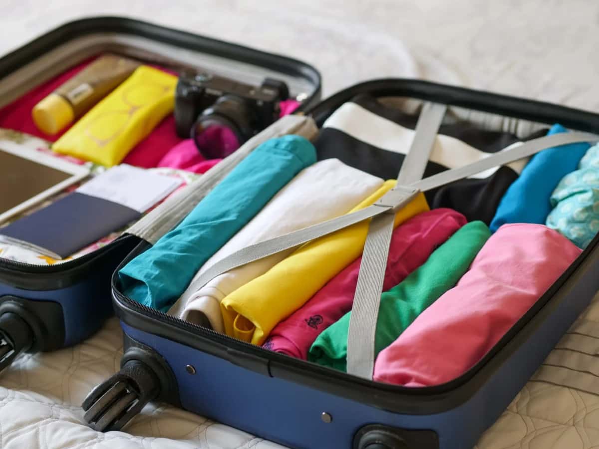 Valise cabine ouverte sur un lit, vêtements roulés et appareil photo