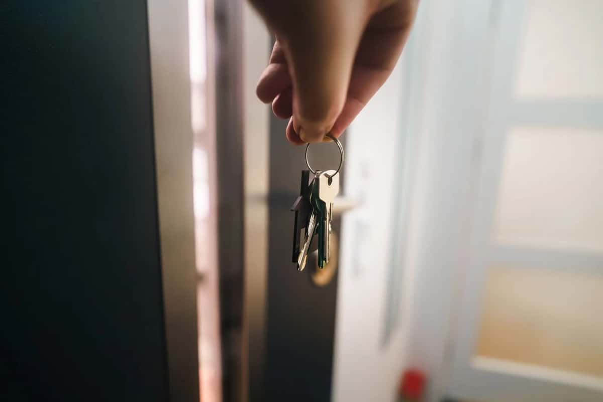 Une main tend un trousseau de clés devant une porte d'entrée