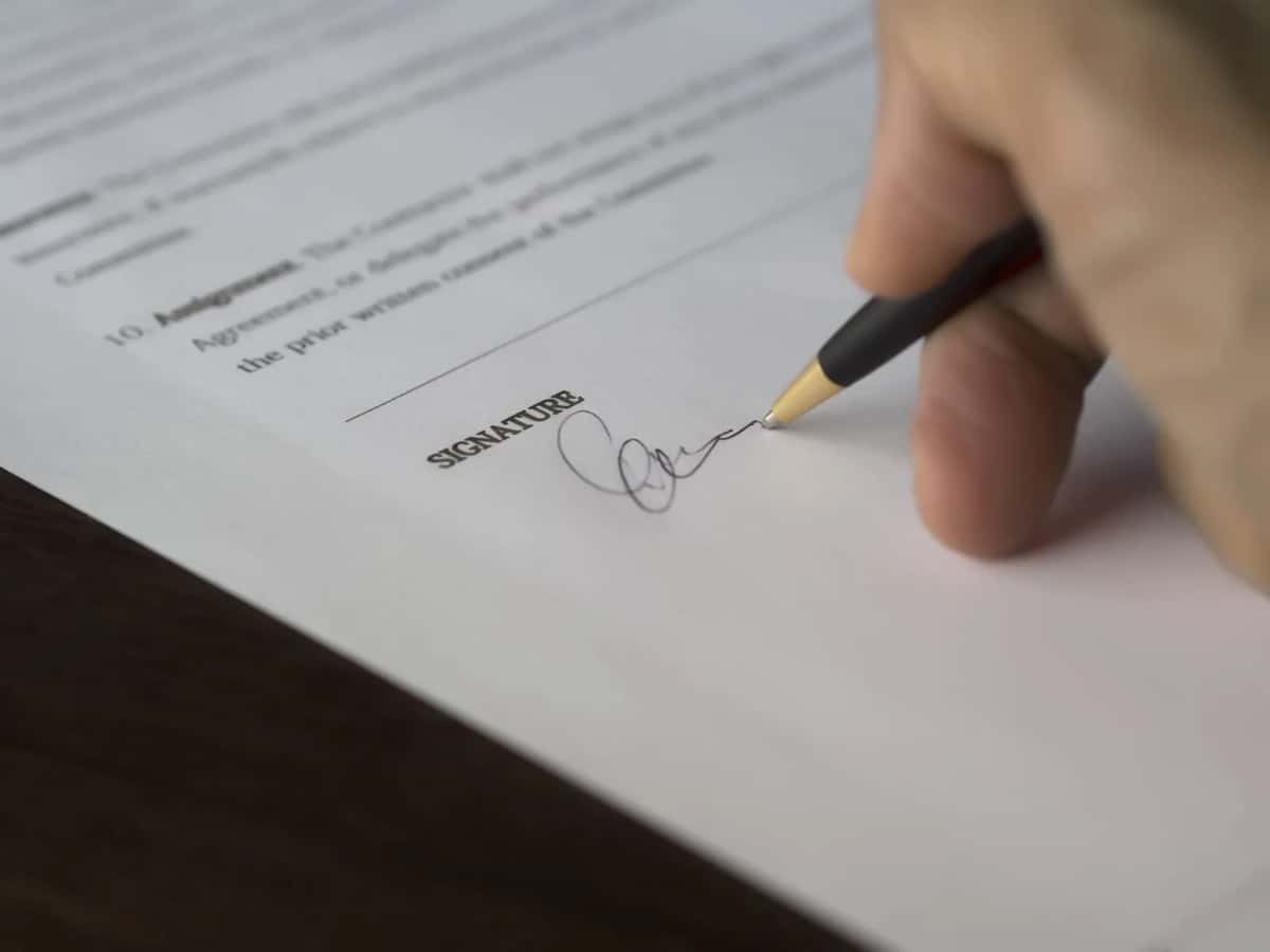 Une main signe un contrat de travail au stylo sur un bureau en bois