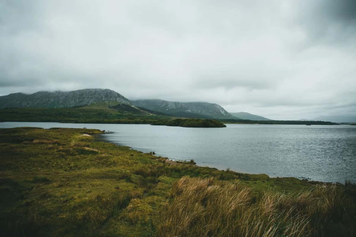 Lac de tourbière du Connemara sous un ciel bas, montagnes au fond